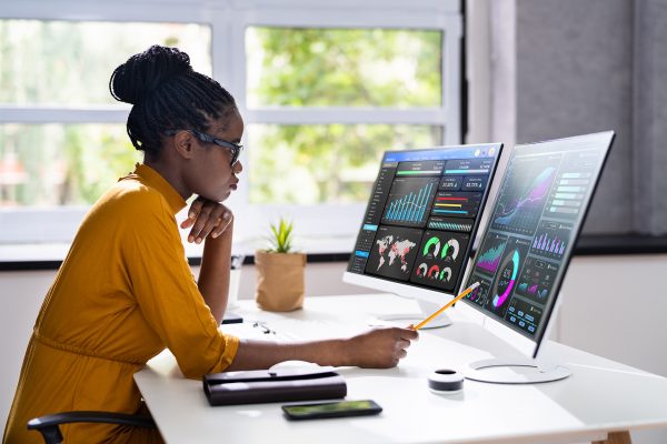 woman sitting in front of 2 computer screens looking at data charts